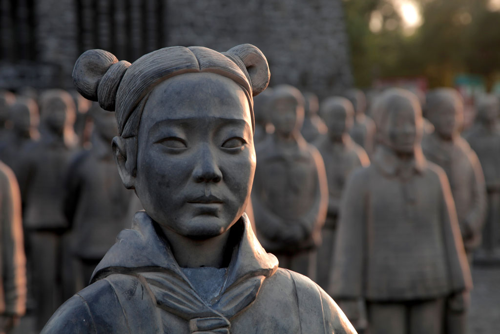 Photograph featuring a close-up of the face of one of the Terracotta Daughters sculptures in the foreground, with countless other sculptures in the background