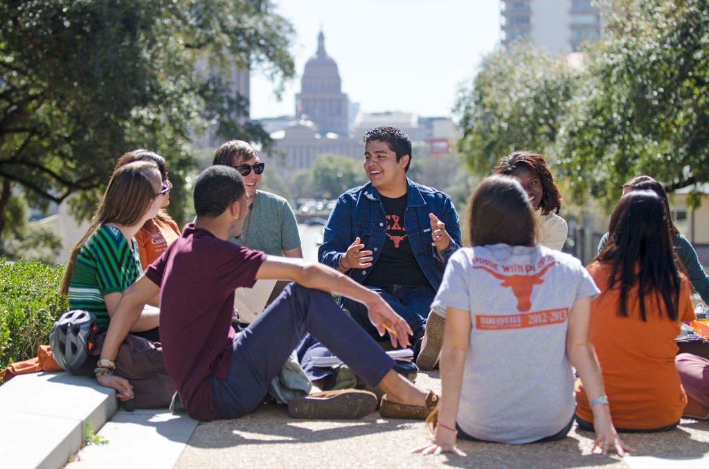 A group of UT Austin students sit in a group talking on the UT Austin campus