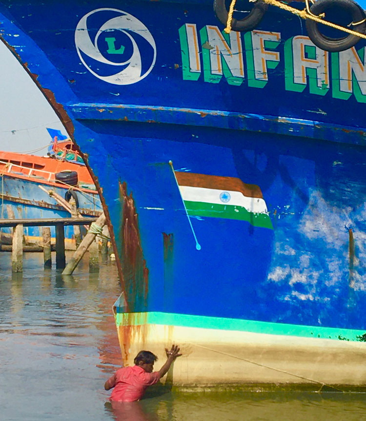 A boatman pushes the bow of the Infant Jesus, a giant blue and red fishing boat. At the front of the craft is painted the Indian flag