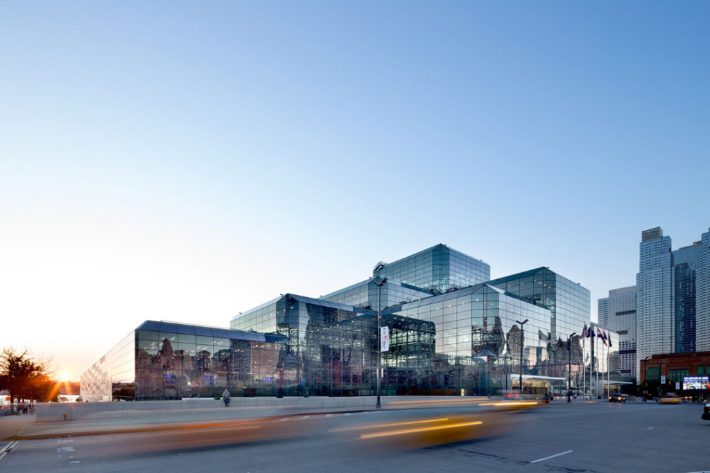 A twilight photograph of the exterior of the Javits Center showing its floor-to-ceiling glass paneling. The bird-safe glass appears fully transparent like any other glass.