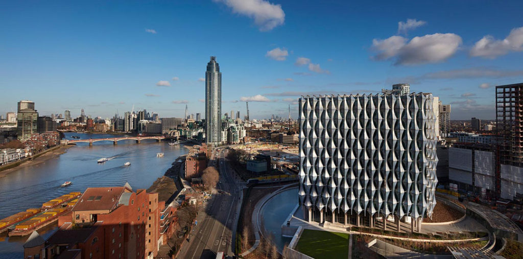 A wide shot of the US Embassy in London showing its location near the Thames River.  The building’s unique design includes a striking diamond-patterned outer envelope. 