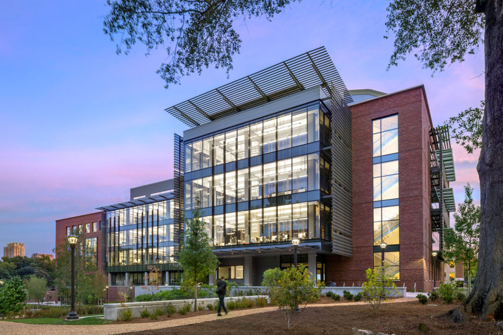 A twilight shot of the exterior of the Krone Engineered Biosystems Building at Georgia Tech.  The brick and metal building has large transparent glass windows that allow sight of staircases, rooms, the people within.