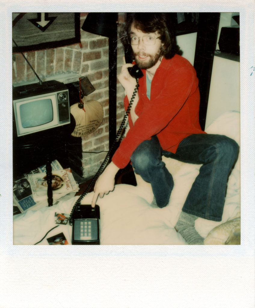 A playful Polaroid photograph of a young Jimmy Wright crouched on top of a bed with a telephone receiver to his ear. One hand extends to the phone’s cradle, as if he has been caught in the act and is about to hang up on the call.