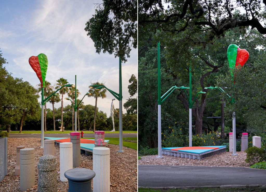 Two views of a large art installation by Jessica Stockholder entitled Save on select landscape & outdoor lighting: Song to mind uncouples. The work is installed here outdoors at the Laguna Gloria at the Contemporary Austin, and we see the grounds’ lawn, palm trees, oaks, and flowers alongside the artwork. The artwork is made up of different components. A heart, half green, half red, is suspended on a lamp post and hovers above everything. Below it are six lights, lighting a bright orange and turquoise triangular platform made from fiberglass and lumber. Off to the side are concrete bollards of different sizes, shapes, and colors, some with splashes of hot pink paint.