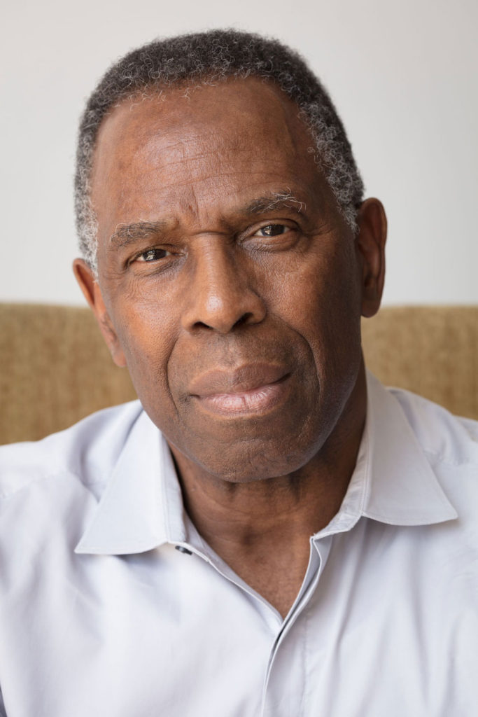 A photograph of the artist Charles Gaines. The portrait shows him from the chest up, wearing a collared shirt, looking straight into the camera with a strong, engaging expression.