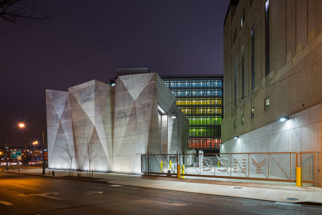 A night time shot of the New York Department of Sanitation Salt Shed and Garage, designed by Claire Weisz and WXY architecture and urban design. The facility is a unique concrete building in the shape of a salt crystal or crumpled piece of paper. 