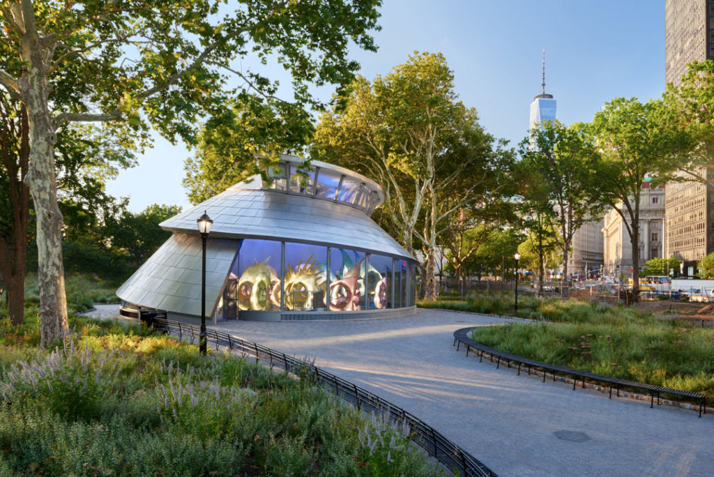 A photograph of the exterior of the SeaGlass Carousel. The building is the shape of a nautilus shell, with stainless steel panels and a glass wall that reveals the carousel which is made up of oversized, beautifully lit fish.