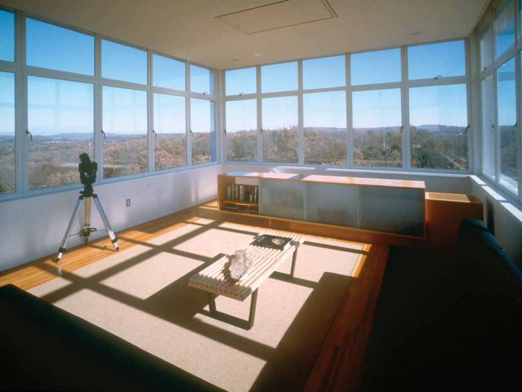 A photograph of the interior of Keenan TowerHouse, designed by Marlon Blackwell Architects.  The room shown features 360-degree views of the surrounding forests.
