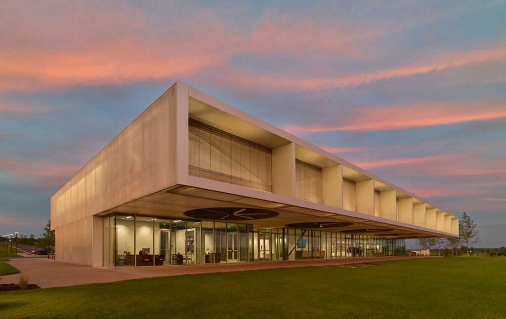 A dramatic sunset shot of the Visitor Center at Shelby Farms Park. We see meeting spaces inside floor-to-ceiling glass walls.