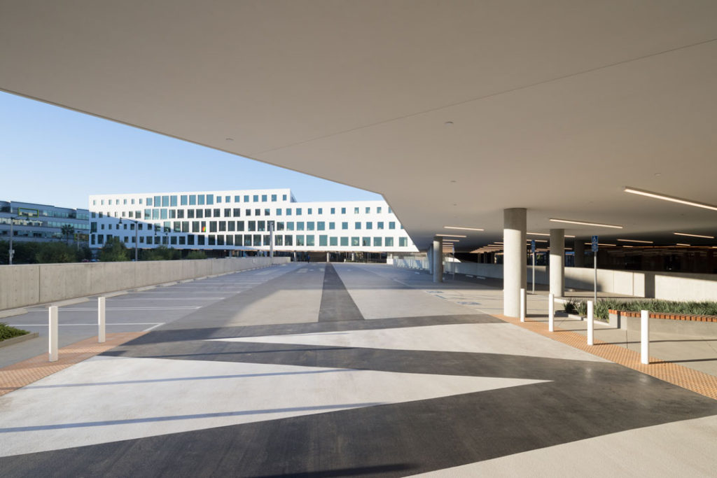 The entrance to the Brickyard at Playa Vista campus, designed by Michael Maltzan. This view is a long angle shot taken on the driveway looking toward a distinctive white building dotted with different sized square windows.